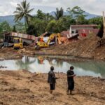 Rescue workers searching through flood-hit and landslide-damaged villages in West Sumatra after Indonesia’s monsoon disaster, with damaged houses and debris in the background.