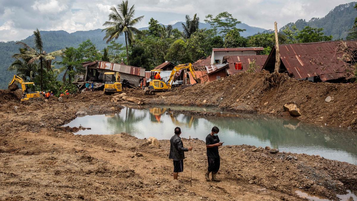 Rescue workers searching through flood-hit and landslide-damaged villages in West Sumatra after Indonesia’s monsoon disaster, with damaged houses and debris in the background.
