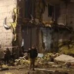 Firefighters and emergency responders at a residential building in Kyiv after Russian drone and missile strikes, showing smoke and damaged structures.