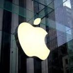 Apple headquarters in Cupertino, California, with employees walking past the main entrance on a clear day.