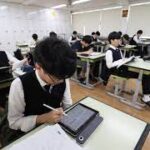 Students using AI-powered digital textbooks in a South Korean classroom, with teachers monitoring laptops and digital screens during lessons.