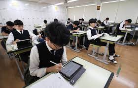 Students using AI-powered digital textbooks in a South Korean classroom, with teachers monitoring laptops and digital screens during lessons.