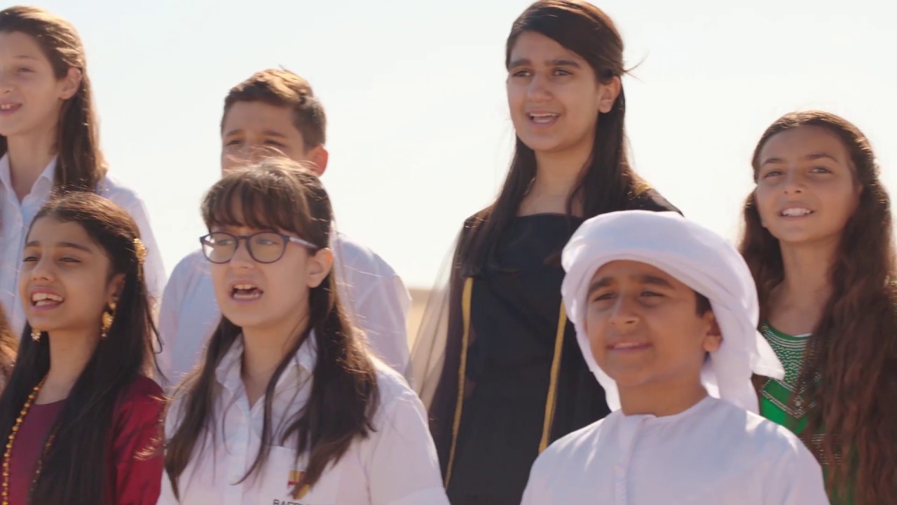 Malayali choir of 132 singers performing UAE national anthem “Eishi Biladi” in four-part harmony at Dubai Flag Garden surrounded by UAE flags.